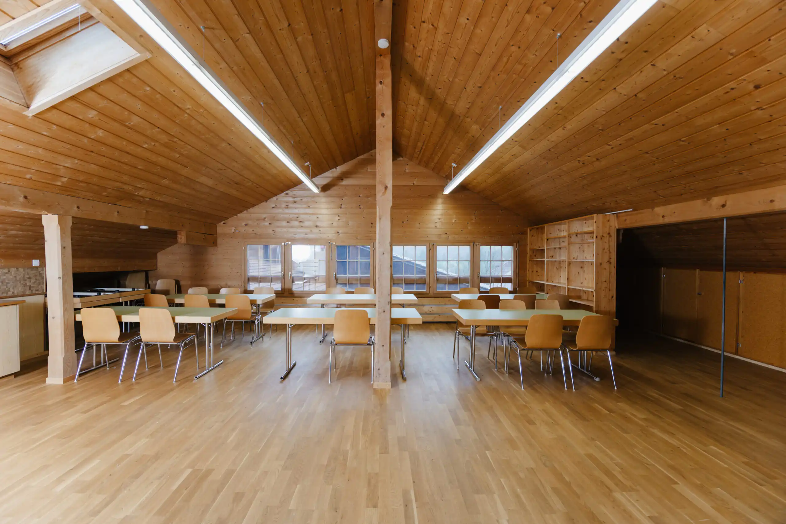 Diemtighuus_Räume-14 Holzgetäfelter Seminarraum mit Tischen und Stühlen für Meetings und Workshops, helle Beleuchtung und große Fenster.