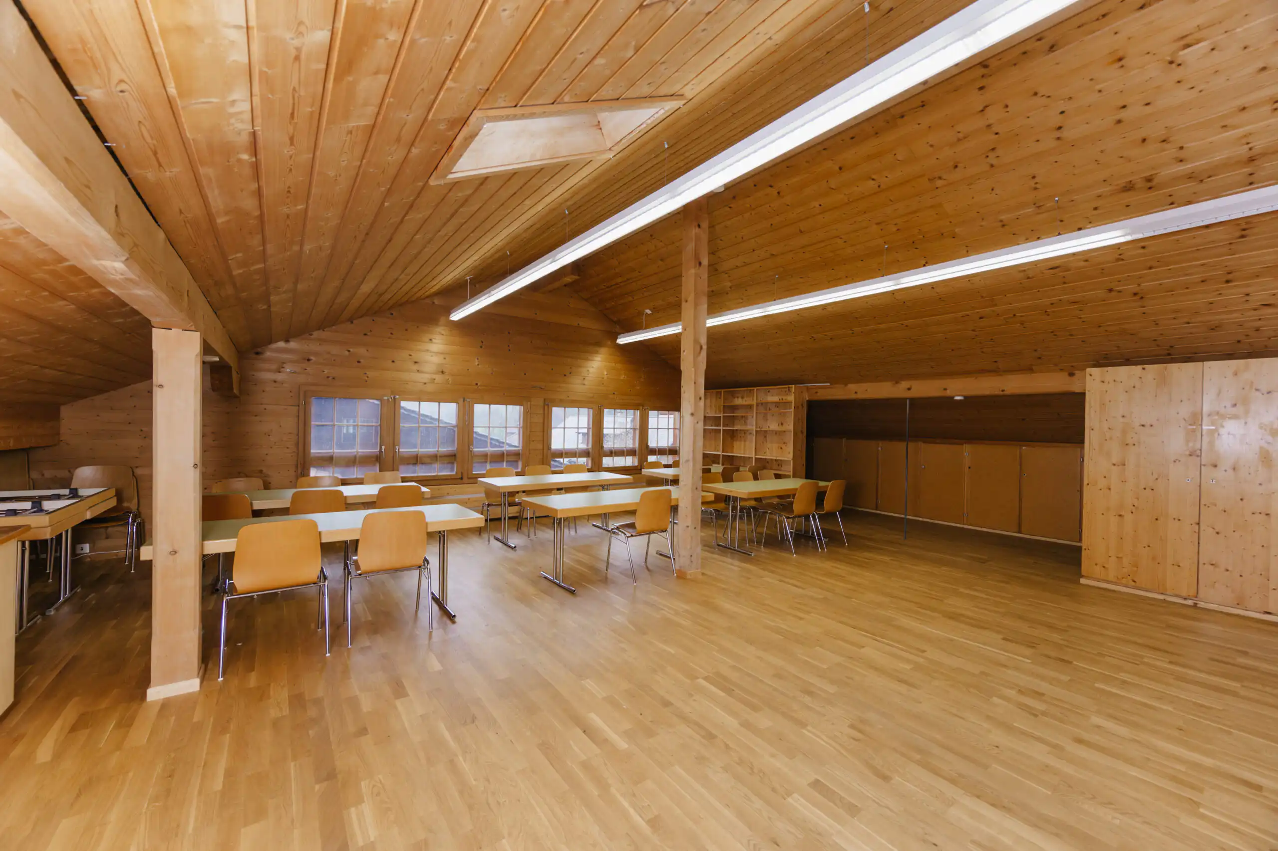 Diemtighuus_Räume-15 Holzvertäfelter Raum mit Stühlen und Tischen, leere Atmosphäre, ideal für Meetings oder Veranstaltungen, Holzdesign.