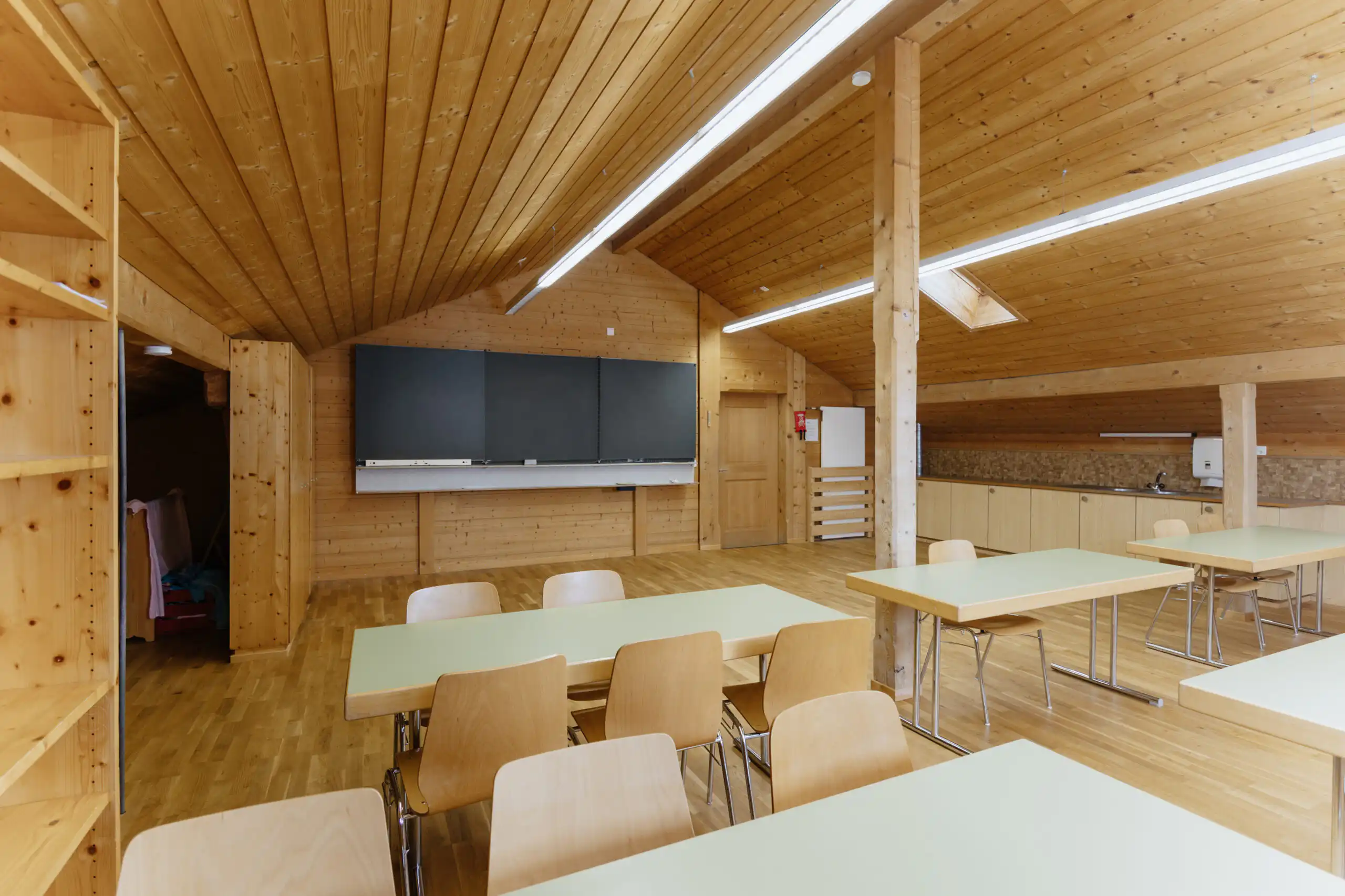 Diemtighuus_Räume-17 Moderner Holzklassenraum mit Tischen, Stühlen und Tafel, ideal für Workshops oder Schulungen.