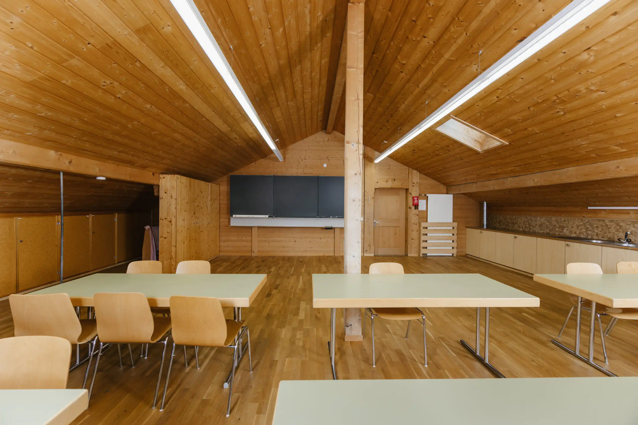 Diemtighuus_Räume-18 Holzvertäfelter Dachboden mit Tischen und Stühlen, ideal für Gruppen- oder Klassenzimmeraktivitäten.