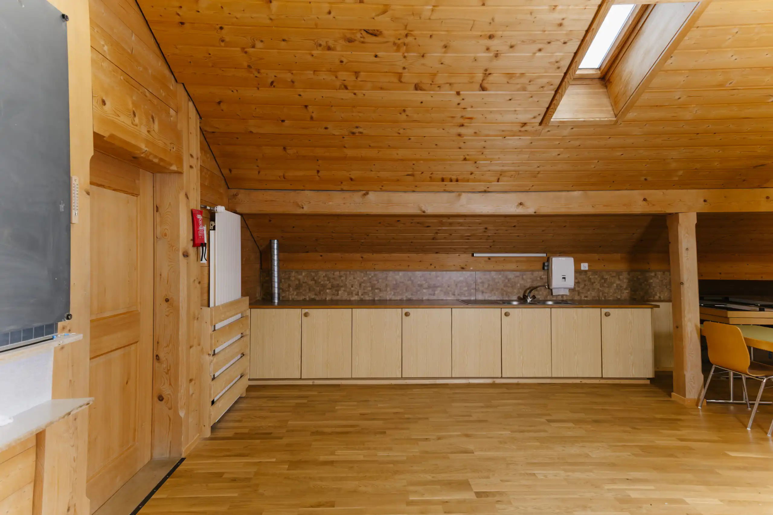Diemtighuus_Räume-19 Minimalistische Holzküche im Dachgeschoss mit Schränken, Dachfenster und Sitzbereich. Moderne und gemütliche Raumgestaltung.