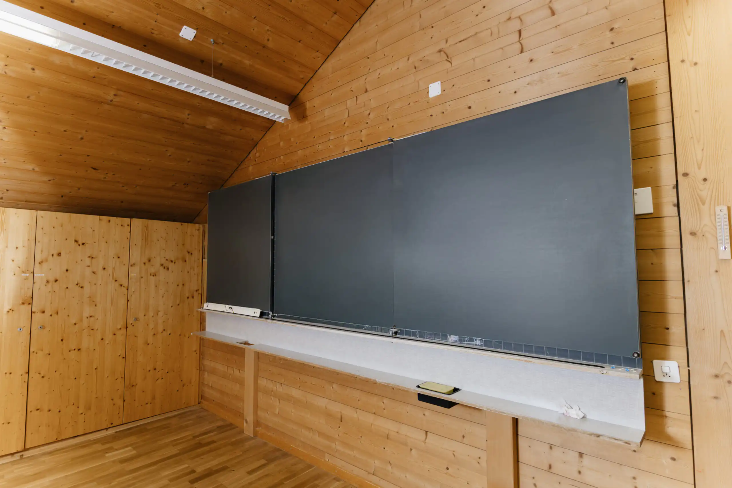 Diemtighuus_Räume-20 Leerer Klassenraum mit Holzverkleidung und großer Tafel an der Wand, ideal für moderne Lernumgebungen.