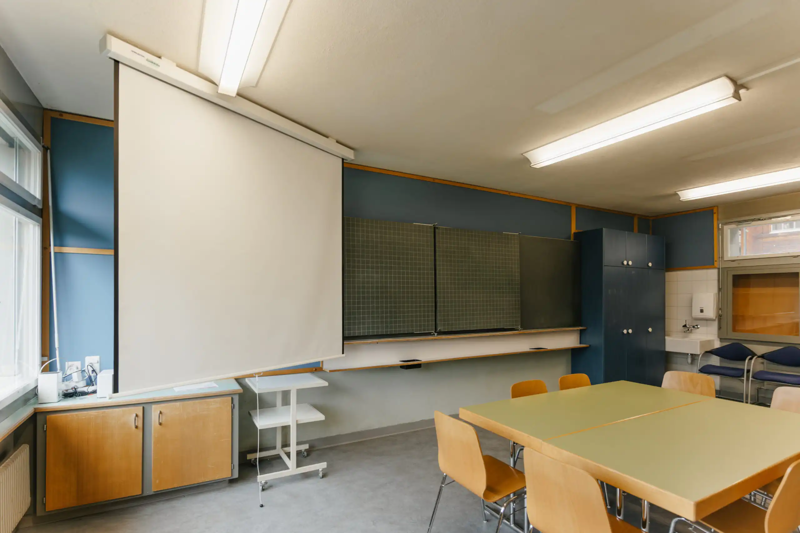 Diemtighuus_Räume-5 Klassenzimmer mit Projektionsleinwand, Schultafeln, Holztisch und Stühlen, ideal für Präsentationen und Unterricht.