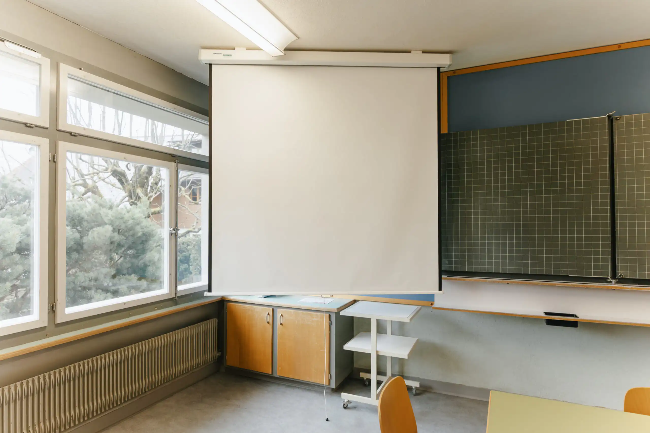 Diemtighuus_Räume-6 Leinwand und Tafel in einem lichtdurchfluteten Klassenzimmer mit modernen Möbeln und großen Fenstern.
