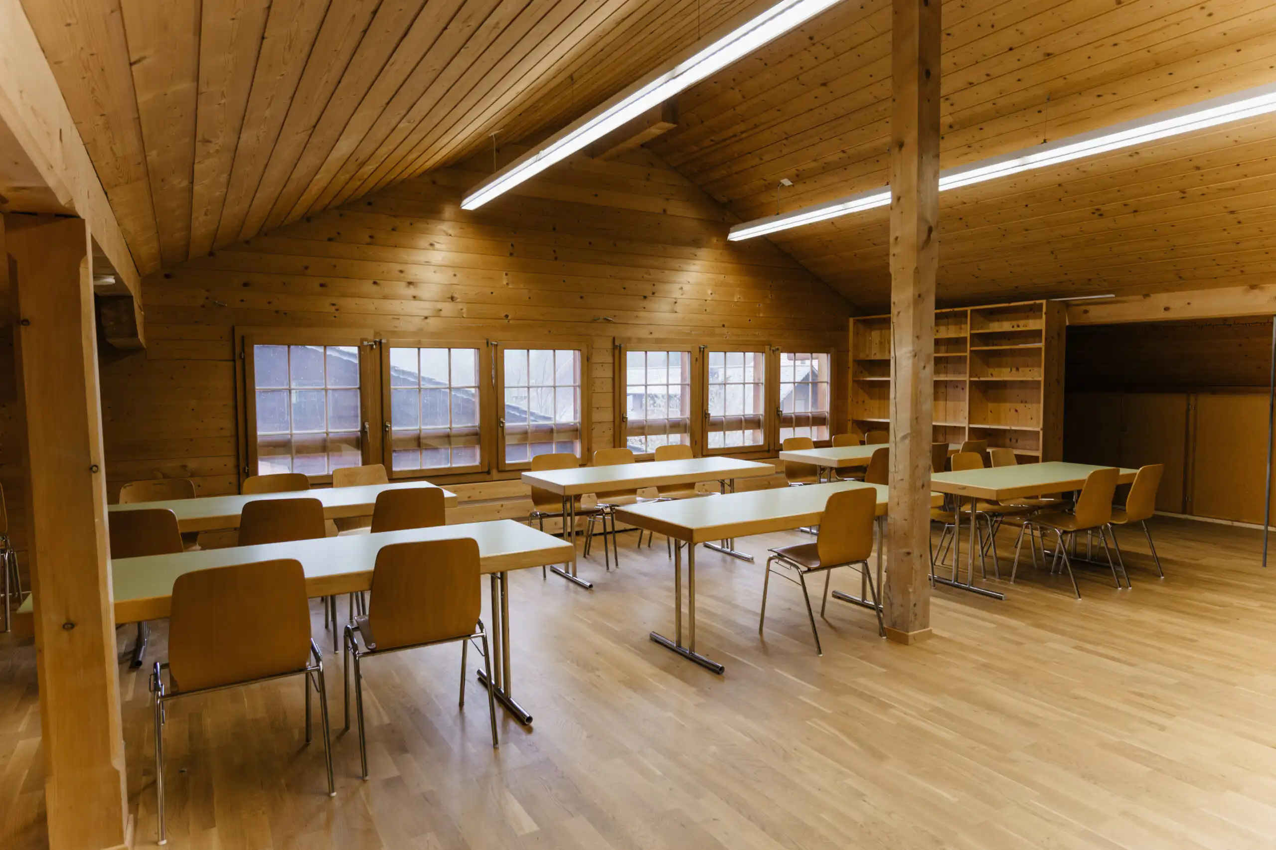 Diemtighuus_Räume-9 Großer, leerer Seminarraum aus Holz mit Tischen und Stühlen, ideal für Workshops oder Meetings.